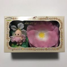 a pink and white flower in a box with an angel figurine next to it