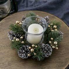 a candle is sitting on top of a table with pine cones and evergreens around it