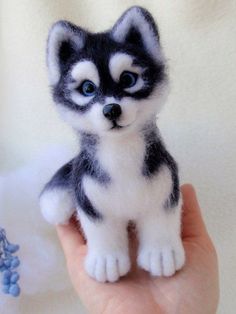 a hand holding a small stuffed husky dog in it's left hand, with blue eyes