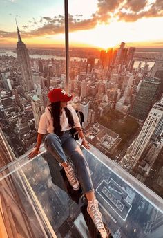 a woman sitting on top of a tall building looking down at the cityscape