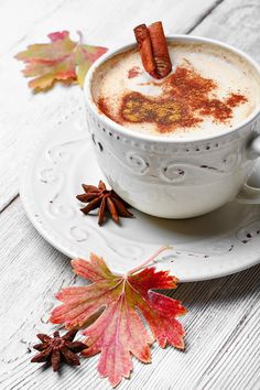 hot chocolate in a white cup with cinnamon sticks sticking out of it and autumn leaves on the side