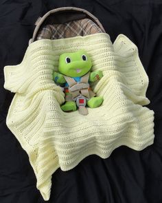 a stuffed turtle sitting in a crocheted blanket on top of a black surface