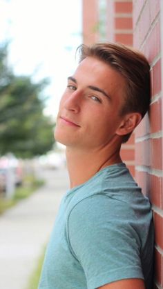 a young man leans against a brick wall and looks up at the sky with his eyes closed