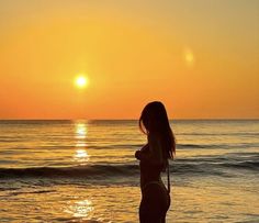 a woman standing on top of a sandy beach next to the ocean at sun set