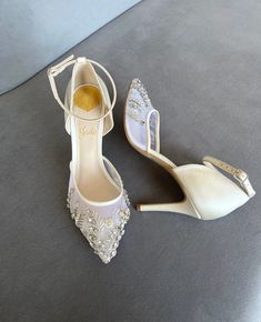 two pairs of white shoes with jeweled details on the heel and ankle straps, sitting on a gray surface