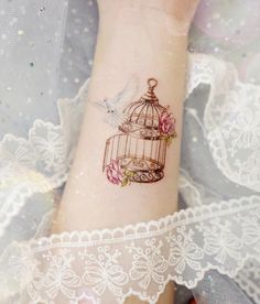 a small birdcage with flowers and a dove tattoo on the wrist is shown