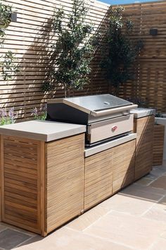 an outdoor bbq grill in the middle of a patio with wooden fence behind it