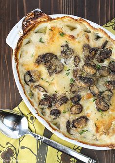 a casserole dish with cheese and mushrooms in it on a yellow napkin next to silverware