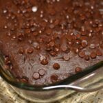 a close up of a chocolate cake in a glass dish on a woven table cloth