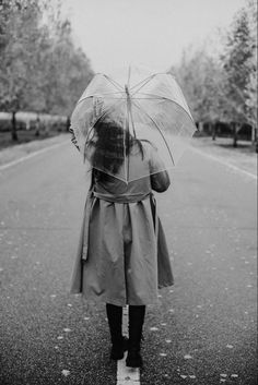 a woman walking down the street with an umbrella over her head, in black and white