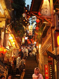 people are walking down the stairs in an alley way at night time with lanterns hanging from the ceiling