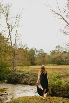 a woman standing on top of a lush green field next to a river in the woods