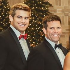 two men in tuxedos standing next to a christmas tree