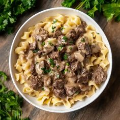 a white bowl filled with pasta and meat covered in gravy on top of a wooden table