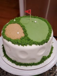 a cake decorated with green grass and a golf hole on the top is white icing