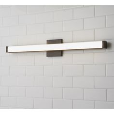 a bathroom light that is on the side of a brick wall in a white tiled room