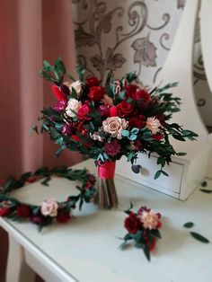 a bouquet of flowers sitting on top of a white table next to a mirror with pink and red flowers in it