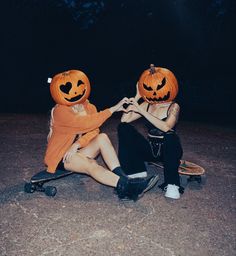 two people sitting on the ground with pumpkin heads