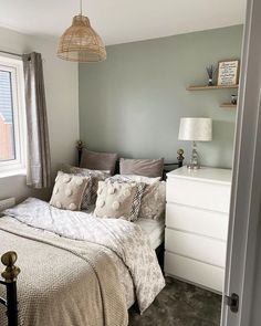 a bed sitting under a window next to a white dresser in a room with gray walls