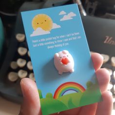 a person holding up a small brooch with a rainbow in the sky on it