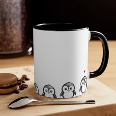 a white and black coffee mug sitting on top of a wooden table next to a spoon