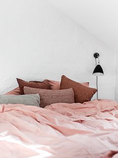 a bed with pink sheets and pillows in a white room next to a black lamp