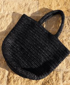 a black handbag sitting on top of a stone floor next to a rock wall