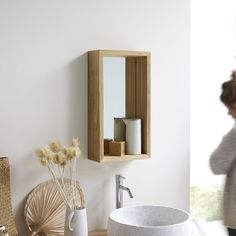 a woman is walking past a sink in a room with white walls and wood accents