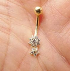 a person is holding a gold nose ring with three small flowers on the end of it