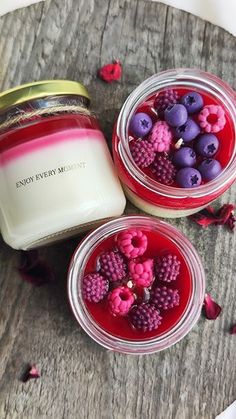 two jars filled with raspberries and blueberries on top of a wooden table