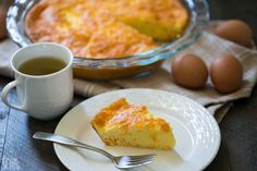 a piece of pie on a plate next to a cup of tea and some eggs