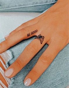 a woman's left hand with a small tattoo on the middle finger that says be good