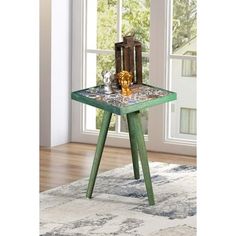 a green table sitting on top of a rug in front of a window with a vase next to it