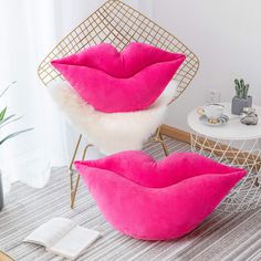 two pink lips shaped pillows sitting on top of a floor next to a chair and table