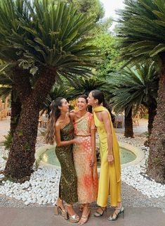 three women standing next to each other in front of palm trees