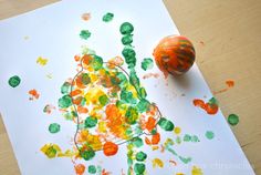 an orange and green ball sitting on top of a piece of paper next to a painting