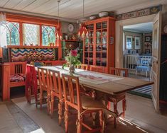 a dining room with orange walls and wooden table surrounded by chairs in front of windows