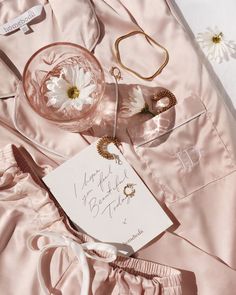 the contents of a pink satin outfit laid out on top of a bed with flowers