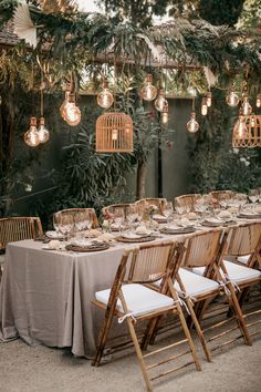 an outdoor dining table set up with chairs and birdcages hanging from the ceiling