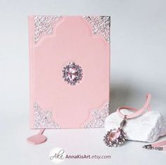 a pink and white wedding card with an embellishment on the front, next to a pair of shoes