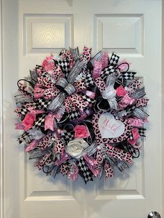 a pink and black wreath on the front door is decorated with ribbons, bows and a monogrammed heart