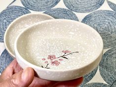 a hand holding a white bowl with pink flowers on it