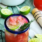 a drink with limes and watermelon garnish on the rim next to other ingredients