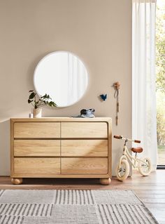 a wooden dresser sitting in front of a window next to a white rug on top of a hard wood floor