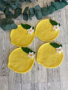 three yellow coasters with white flowers and green leaves on the floor next to plants