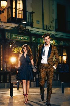 a man and woman are walking down the street at night in front of a building