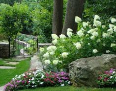 a garden with flowers and rocks in the grass next to trees, shrubs and bushes