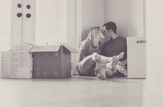 a man and woman sitting on the floor next to boxes with their faces close together