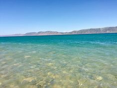 the water is crystal clear and blue with mountains in the backgroung area