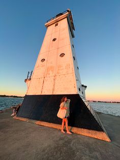 a woman standing in front of a tall tower next to the ocean